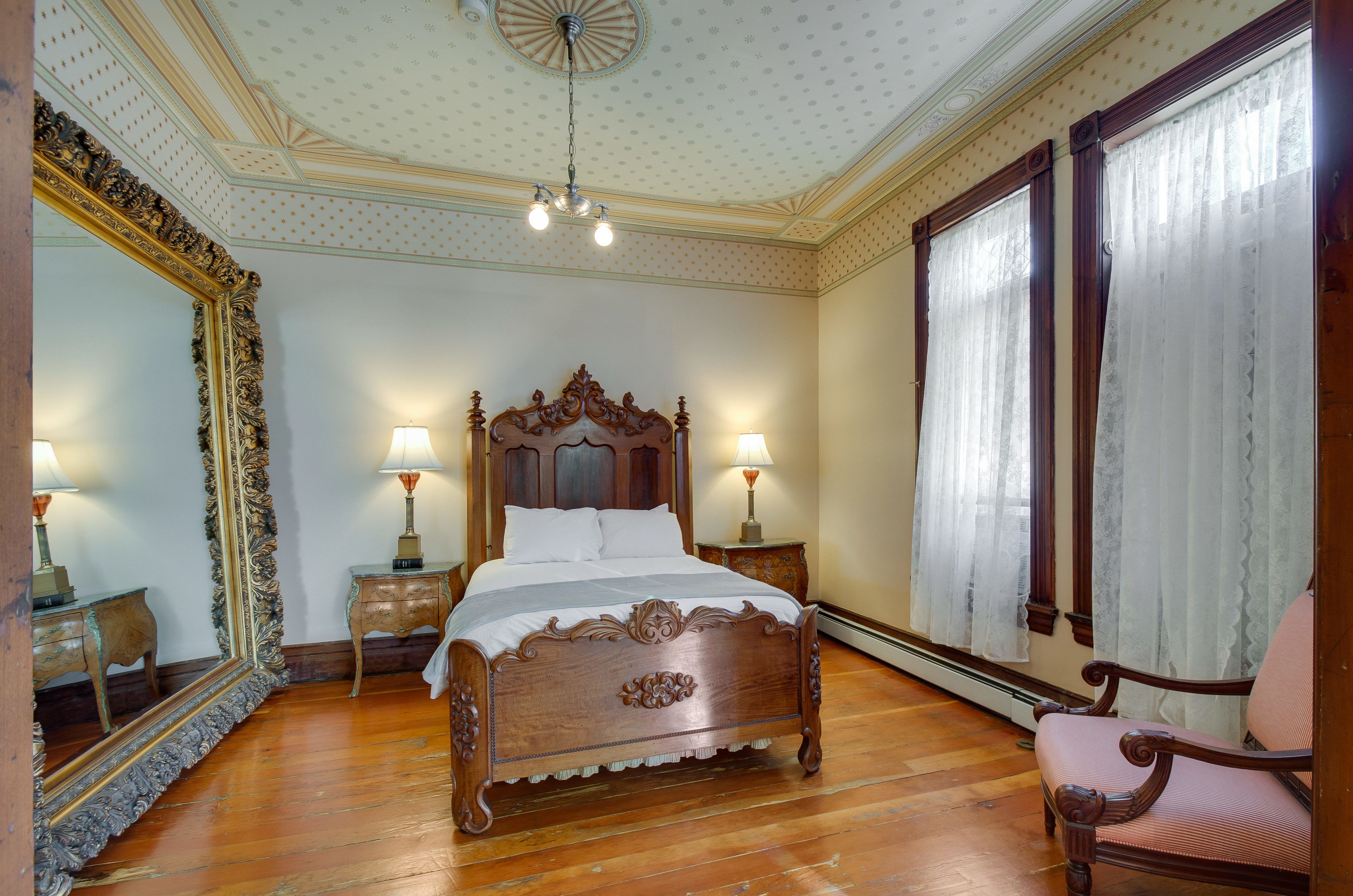 A bedroom with a wooden bed, two bedside tables with lamps, a large mirror, and a window with curtains.