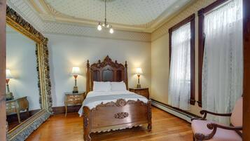 A bedroom with a wooden bed, two bedside tables with lamps, a large mirror, and a window with curtains.