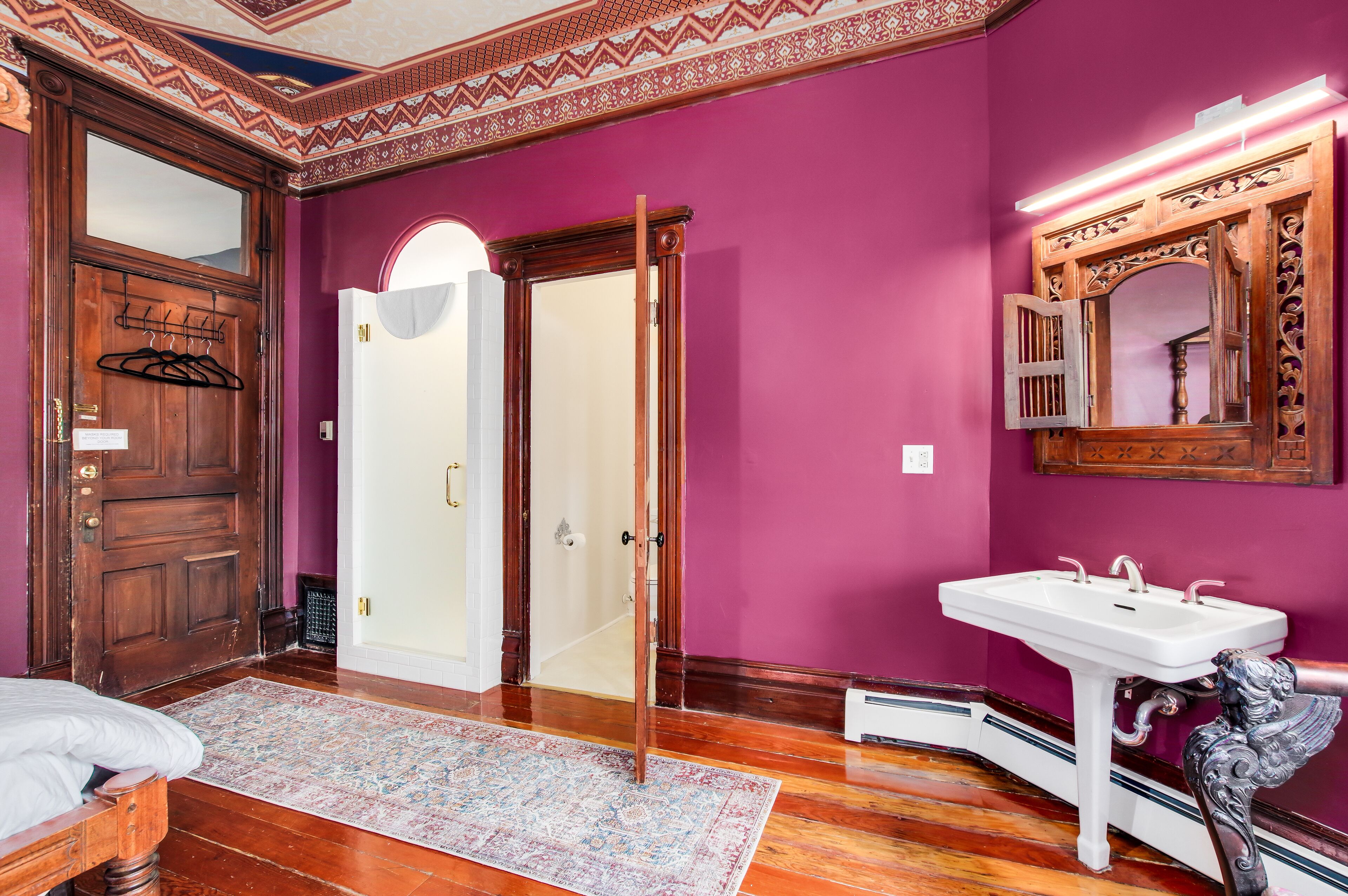A room with a wooden door, a white sink, and a mirror with ornate details.