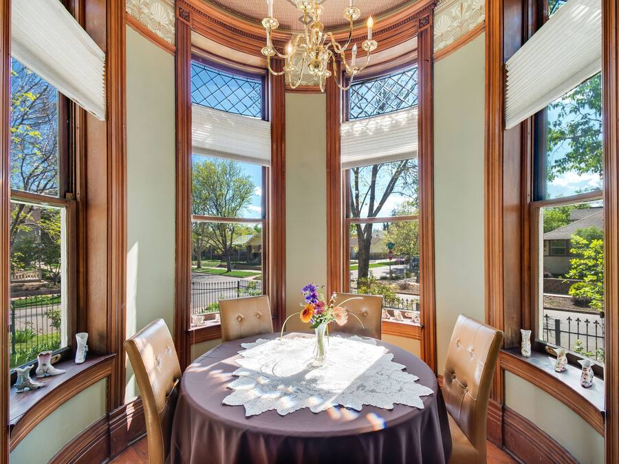 Comedor con una mesa redonda, sillas, una araña y ventanas grandes con vistas a un parque.