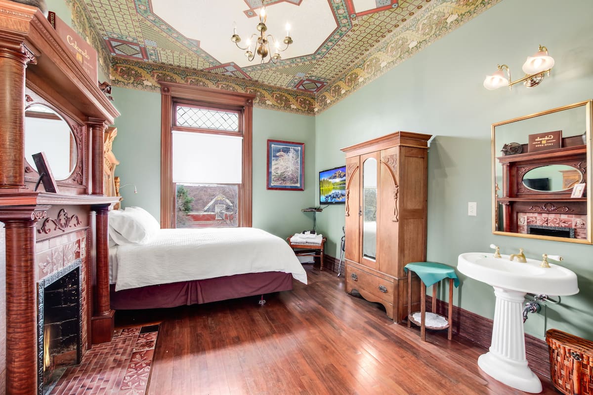 A room with a bed, a wooden cabinet, a large mirror, and a fireplace.