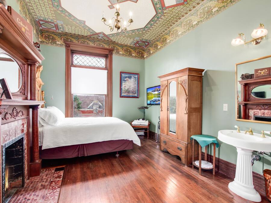 Una habitación con cama, un armario de madera, un espejo grande y una chimenea.