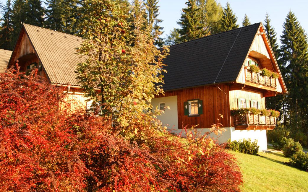 Un chalet en bois doté d’un toit à pente, d’un balcon orné de plantes et d’un jardin bien entretenu.