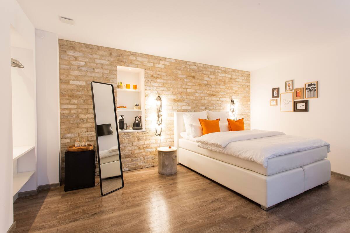 Ein modernes Schlafzimmer mit einer Ziegelwand, einem weißen Bett und einem kleinen Nachttisch.