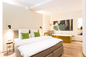 Relax in a serene space with a large bed, a bathtub, and a unique abstract art piece.