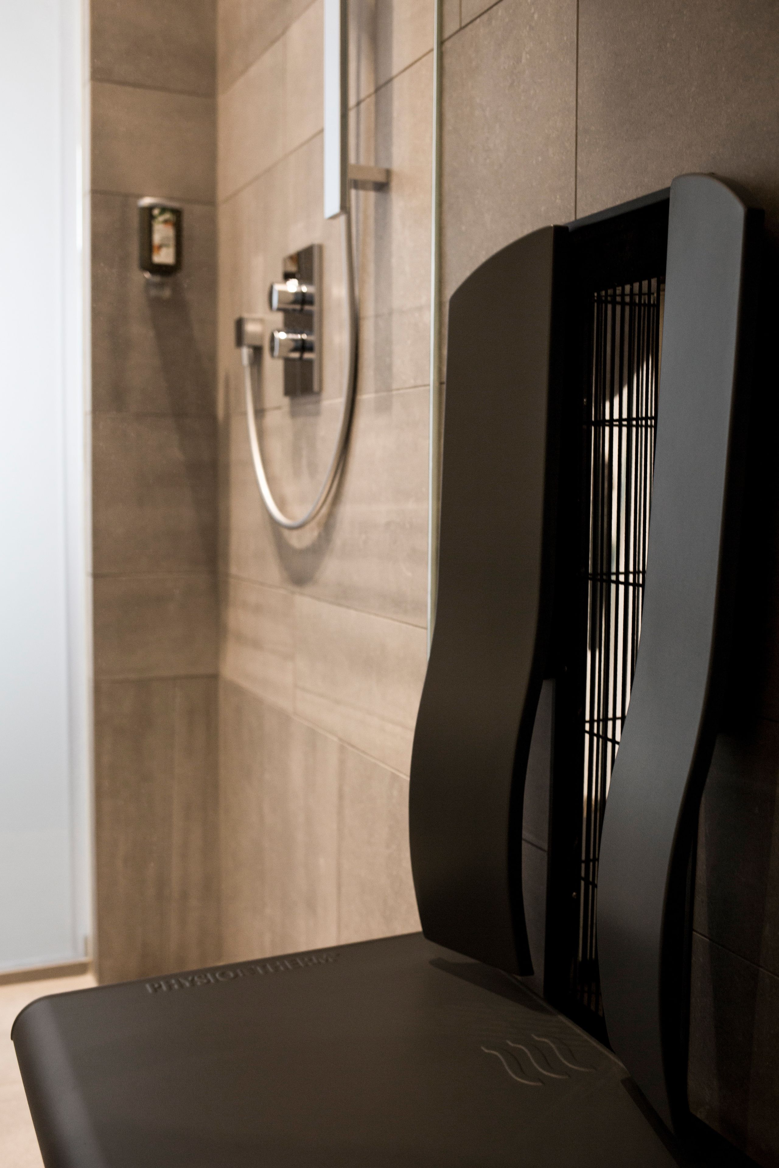 Ein modernes Badezimmer mit Dusche, einem schwarzen Stuhl und einer Wandtoilette.