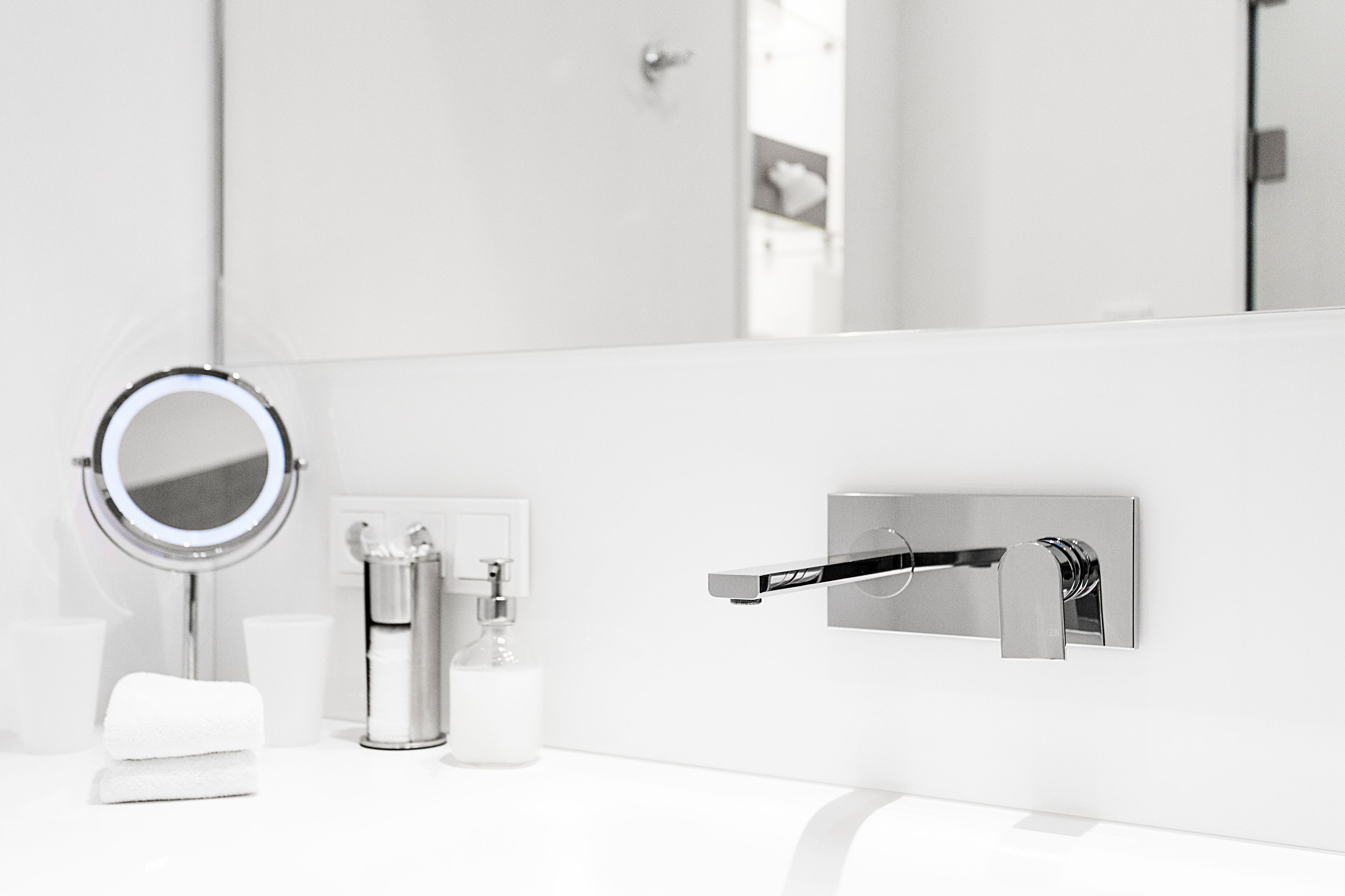 A modern bathroom with a white sink, a round mirror, a soap dispenser, and a towel.