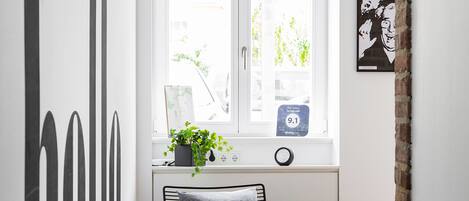 A narrow hallway with a white door, a window with a view of greenery, a black metal bench with a pillow, and a wall with large black letters.