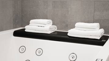 A modern bathroom with a bathtub, two sets of neatly folded white towels, and a control panel with buttons.