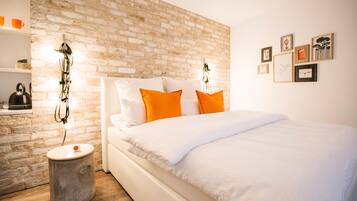 A bedroom with a brick wall, white bedding, and orange pillows.