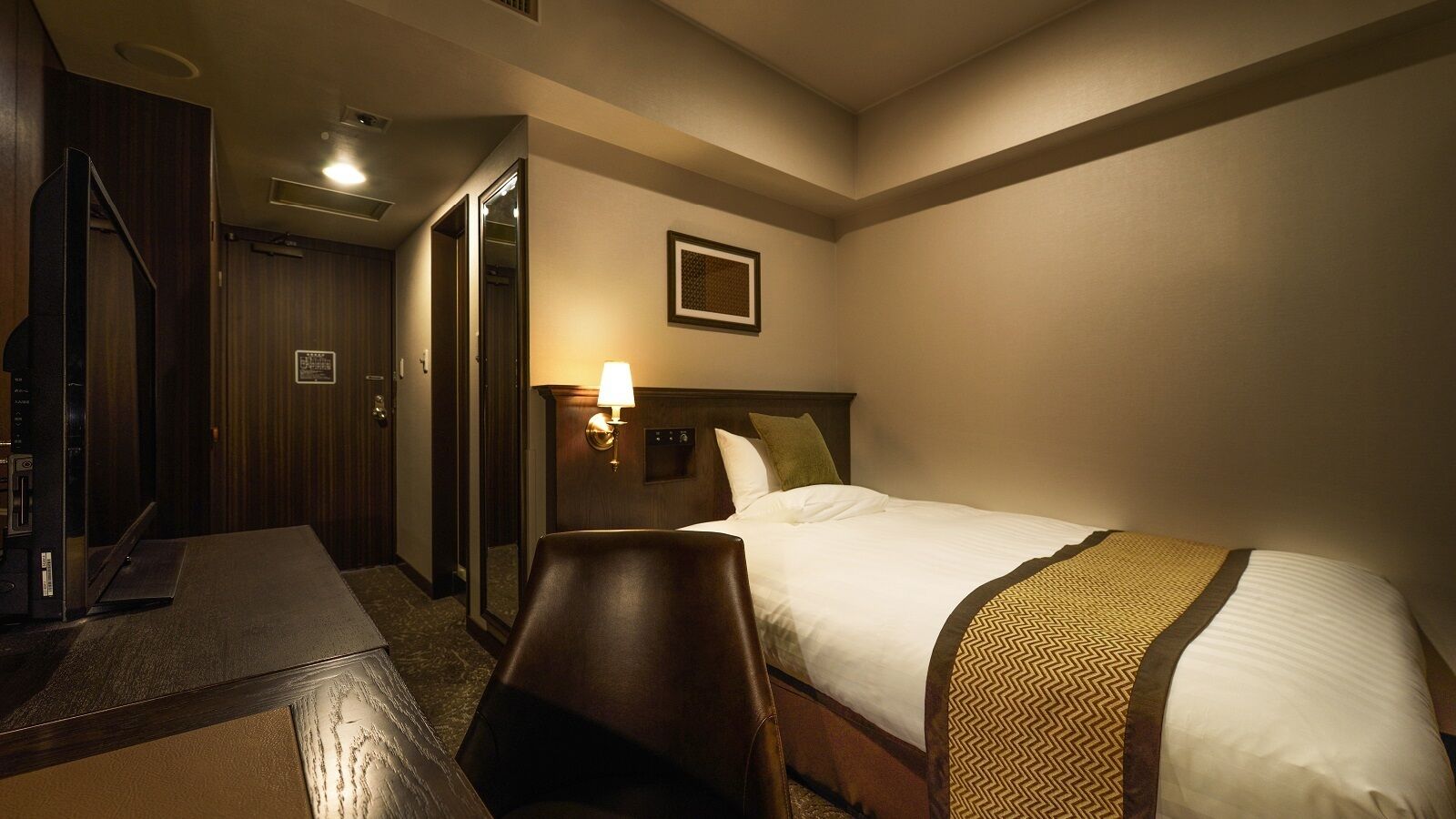Une chambre d’hôtel avec un lit, un bureau, une chaise, une lampe et un miroir.
