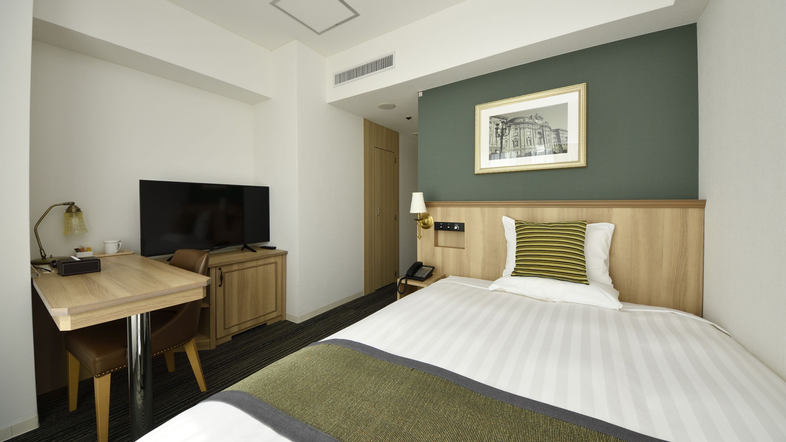 Une chambre d’hôtel avec un lit, un bureau avec une télévision, un téléphone et un tableau encadré au mur.