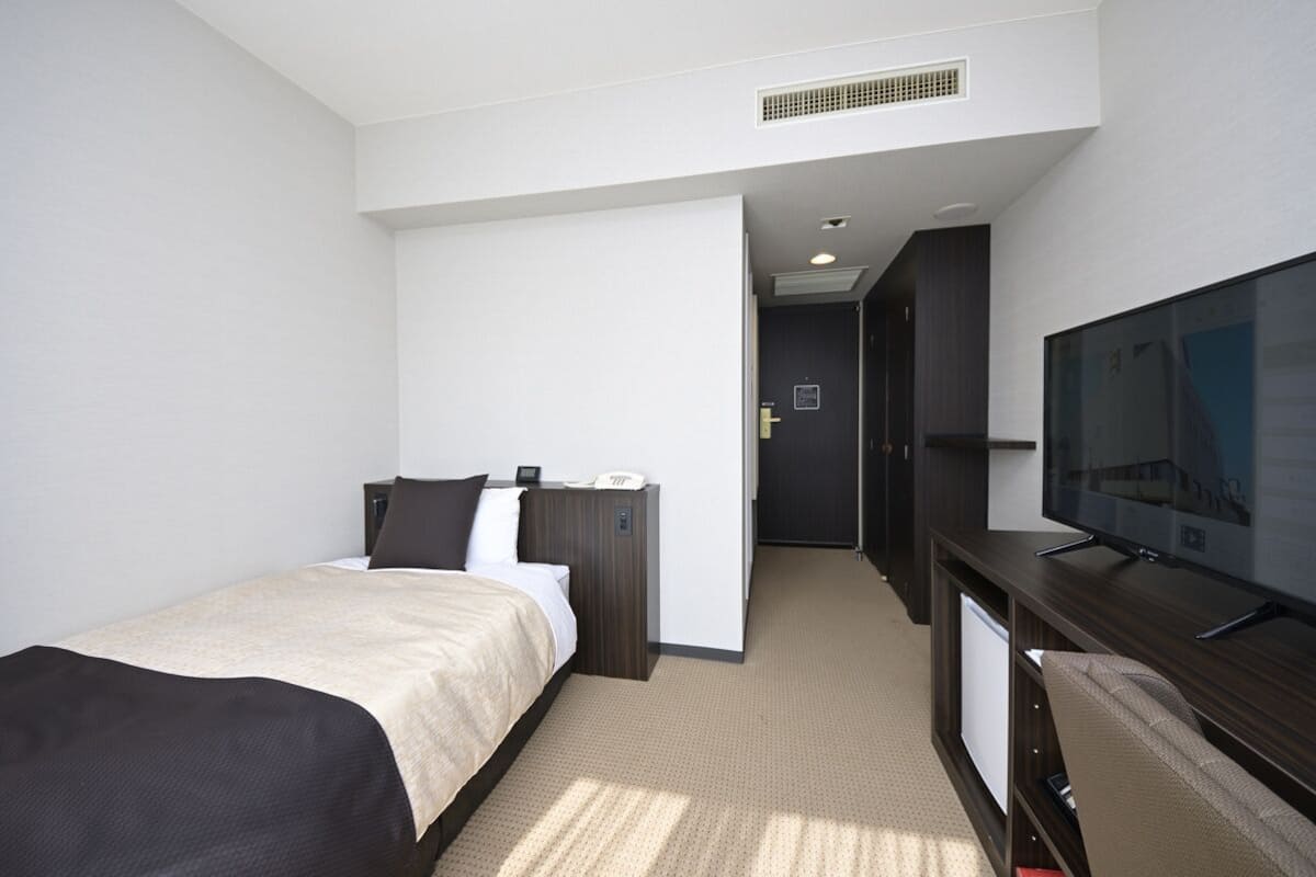 A hotel room with a bed, a desk with a television, and a door leading to another room.