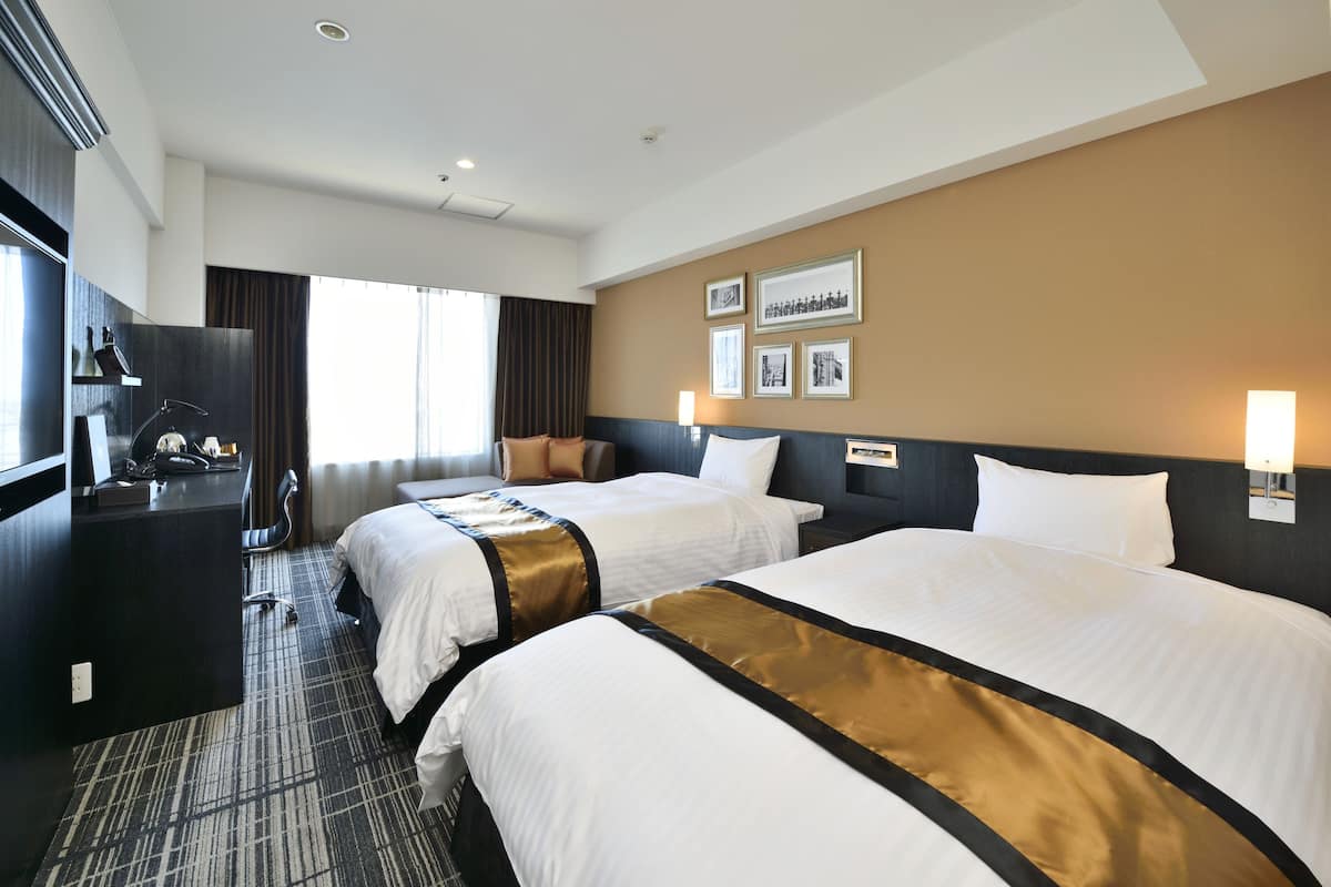 A hotel room with two beds, a desk, a chair, and a large window.