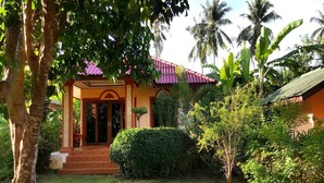 A house with a red roof, surrounded by lush greenery and palm trees. - Happy Resort (Khanom)
