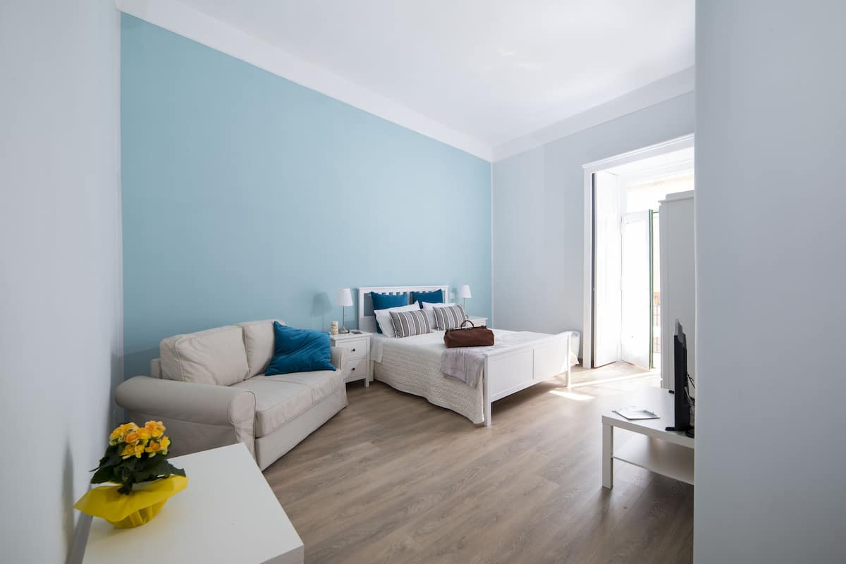 Quarto moderno com cama, sofá, mesa de cabeceira e televisão.