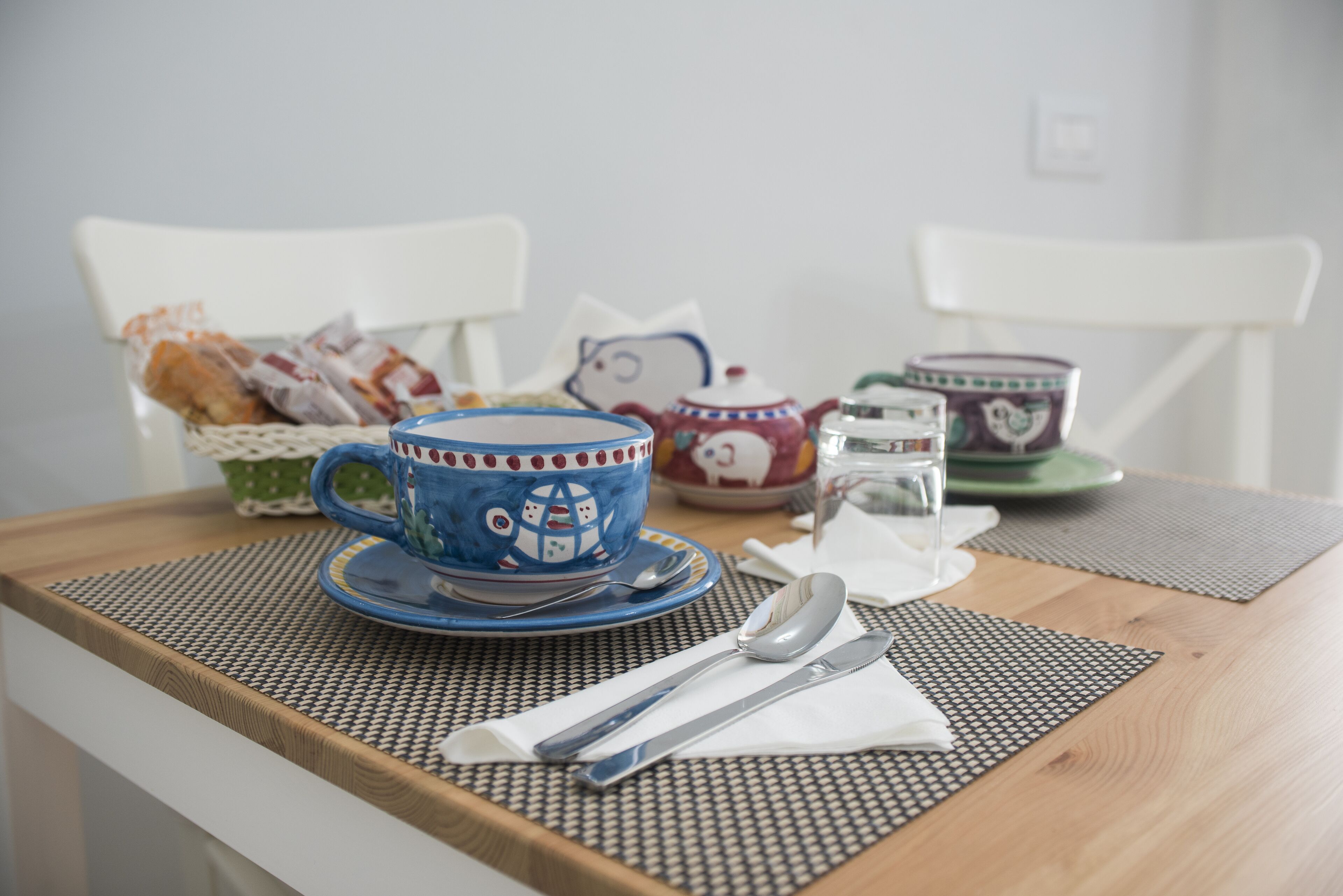 Un tavolo da pranzo con una tazza blu, un teiera e un bicchiere d'acqua.