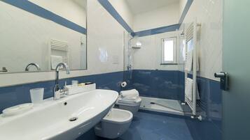 A bathroom with a sink, toilet, bidet, and glass-enclosed shower.