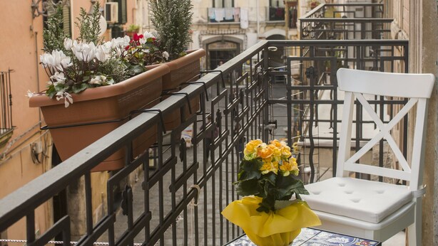 Une rue étroite, bordée de bâtiments des deux côtés, une chaise blanche et une table sur laquelle est posé un vase de fleurs.