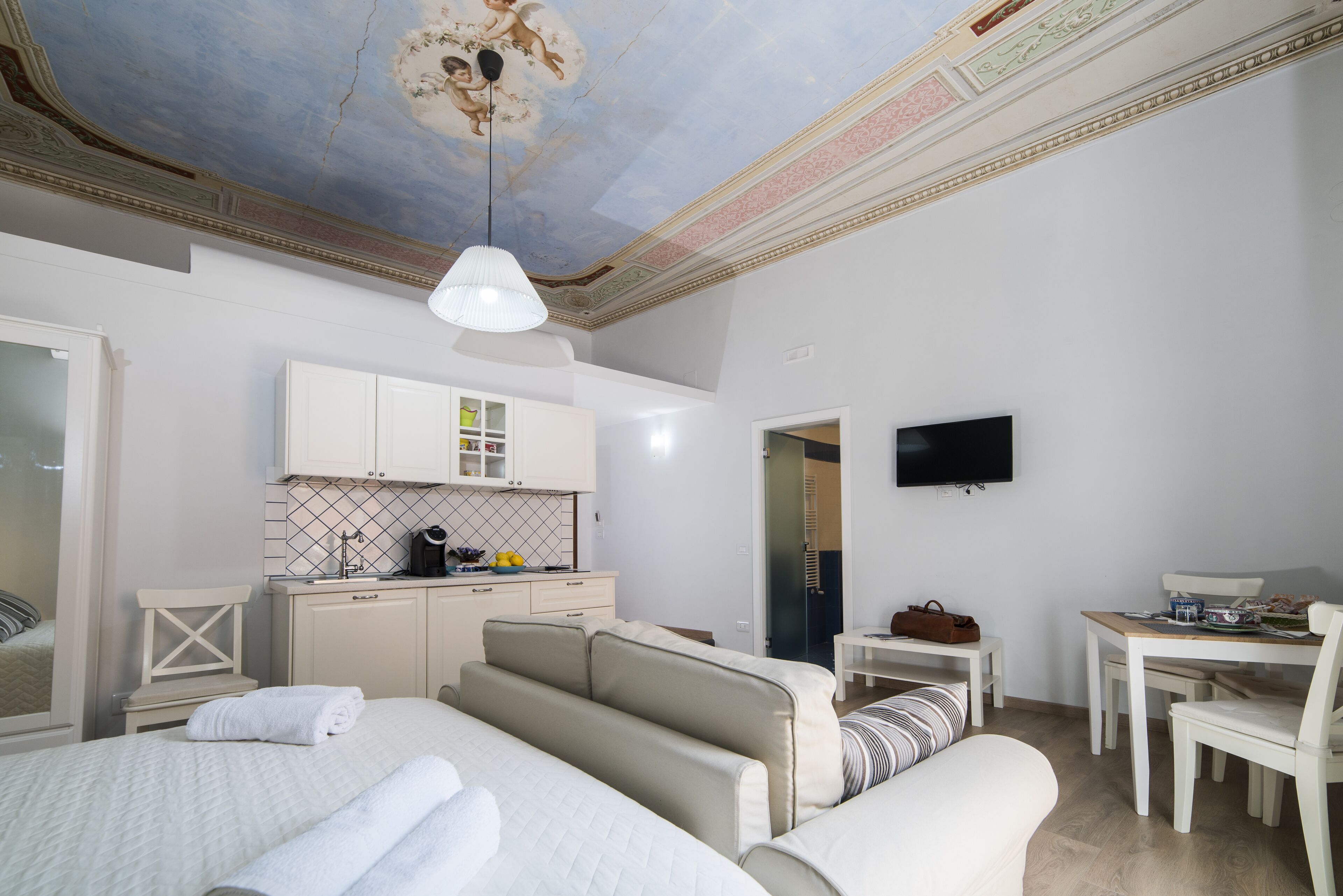 A modern hotel room with a large bed, a sofa, a dining area, and a kitchen.