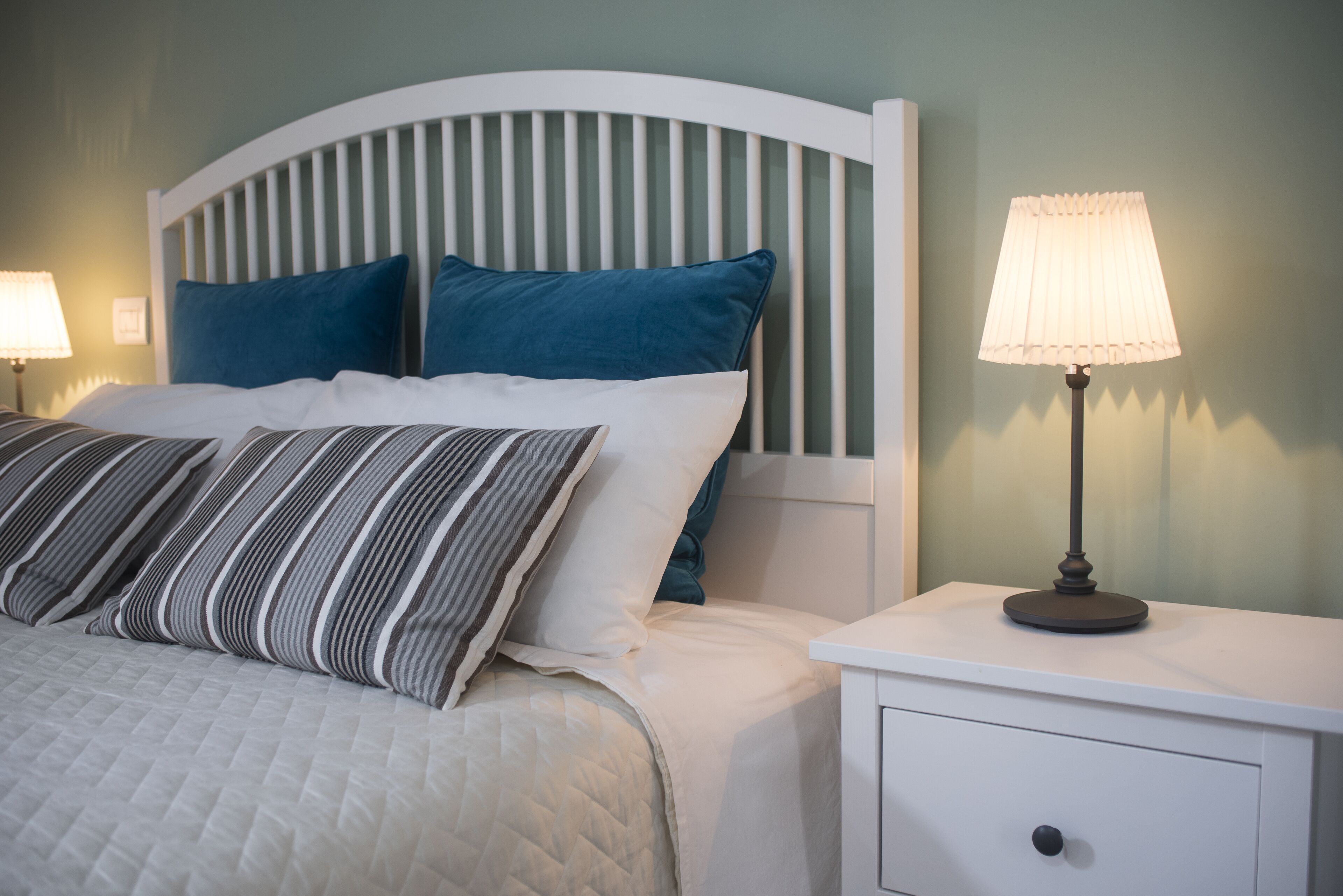 A neatly made bed with striped and solid pillows, a white headboard, and a bedside table with a lamp.
