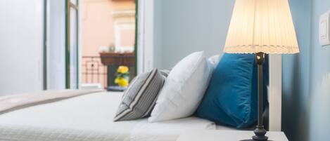 A neatly made bed with a white duvet and pillows, a bedside table with a lamp, and a magazine.