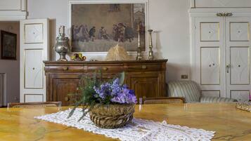 Une table à manger ornée d’un panier tressé rempli de fleurs, d’un chemin de table en dentelle et d’un tableau accroché au mur au-dessus.