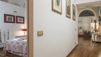 Ein Flur mit gerahmten Bildern an der Wand, ein Bett mit floralem Überwurf und ein Tisch mit einer Statue.