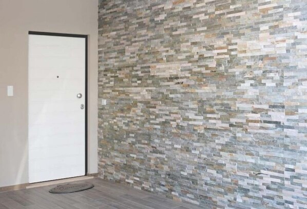 Una habitación con una puerta blanca, pared de piedra texturizada y suelo gris.