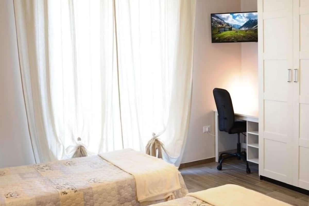 Ein Schlafzimmer mit zwei Betten, einem Schreibtisch und einem Fernseher an der Wand.