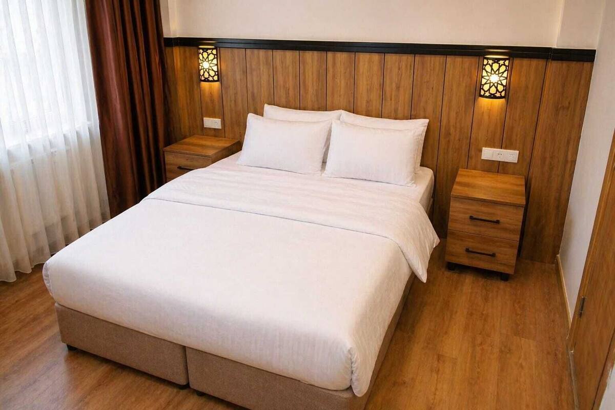 A bedroom with a wooden headboard, two bedside tables, a bed with white linens, and a nightstand with a lamp.