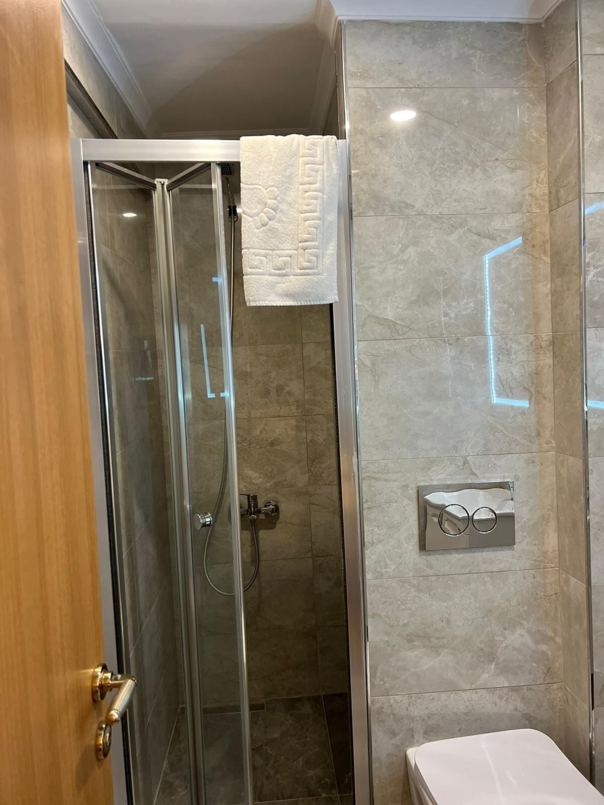 A glass-enclosed shower with a towel hanging on the wall, a toilet, and a wall-mounted control panel.
