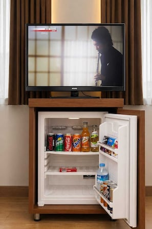 A television on a wooden stand with a refrigerator below it, containing various beverages and snacks. - Hotel Rio (Istanbul)