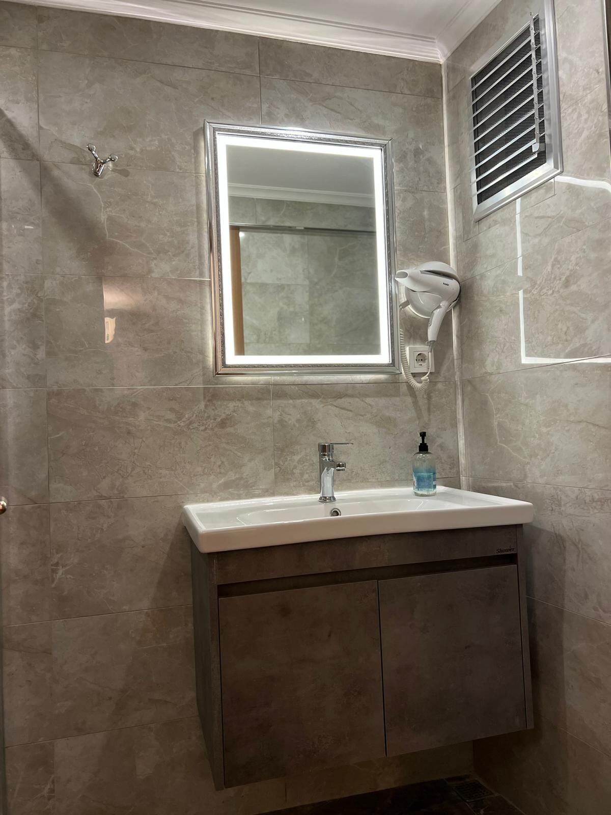 A bathroom with a vanity, a mirror, a handheld showerhead, and a window.
