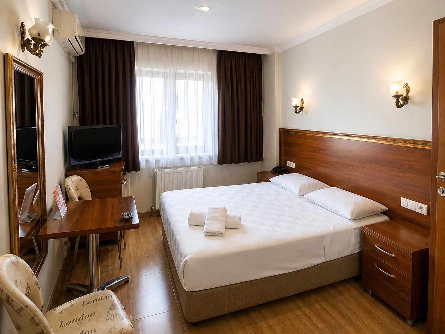 A hotel room with a bed, bedside tables, a desk with a chair, a television, and a window with curtains.