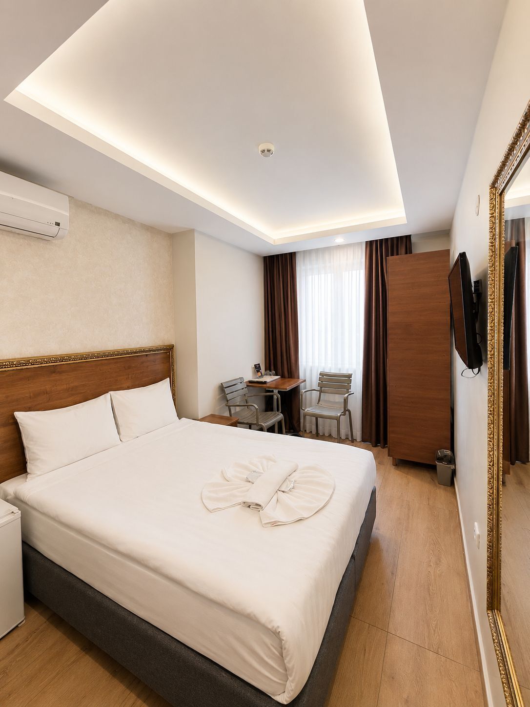 A hotel room with a bed, a desk, two chairs, a TV, and a mirror.