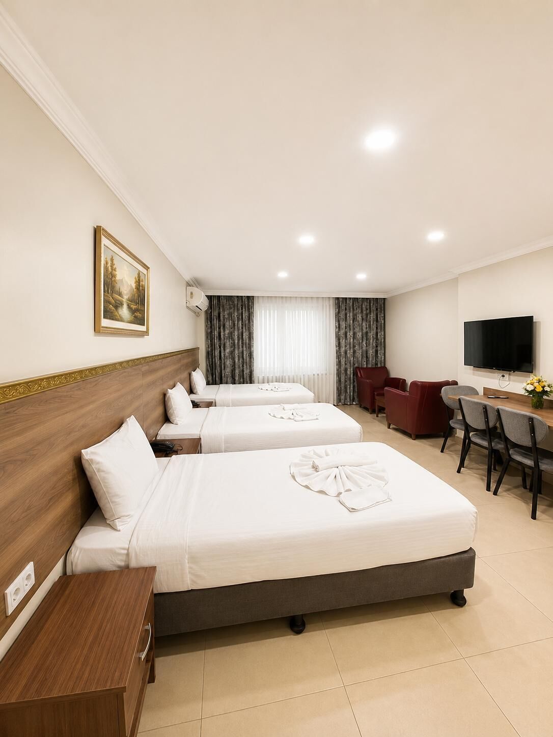 Camera d'albergo con tre letti, una scrivania, una TV e un quadro appeso al muro.