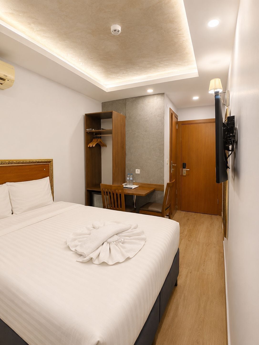 A hotel room with a bed, a desk, a wardrobe, and a wall-mounted TV.
