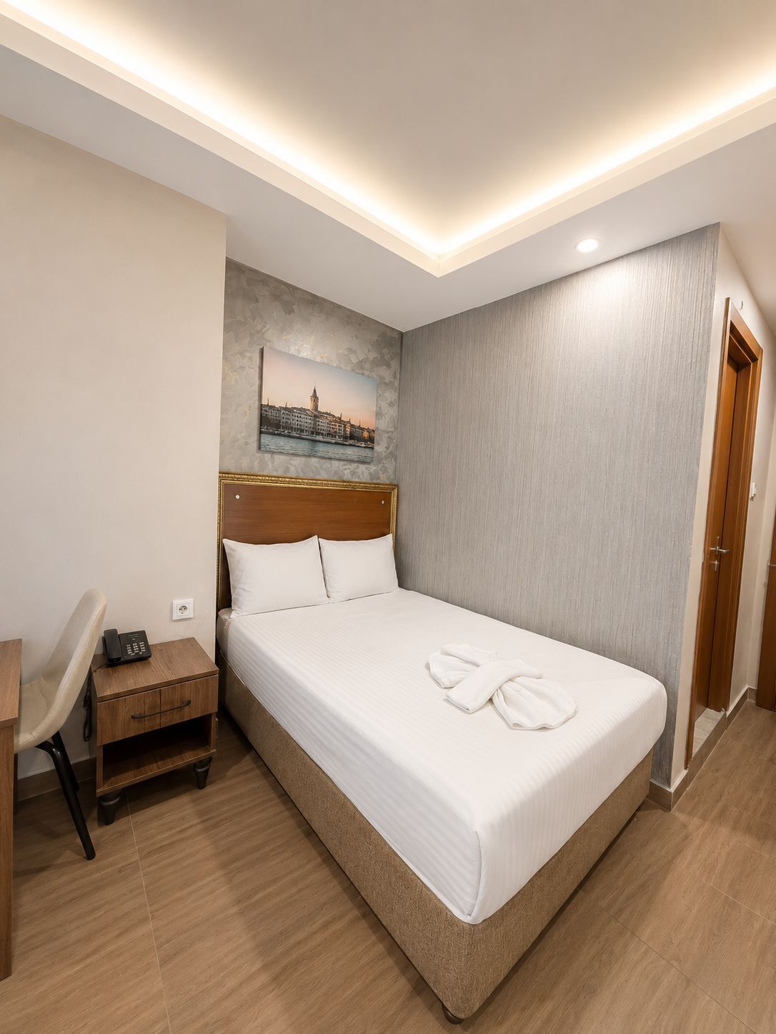 A hotel room with a bed, bedside table, chair, and a painting on the wall.