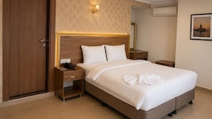 Una habitación de hotel con cama, mesita de noche, lámpara de pared, aire acondicionado y un cuadro enmarcado.