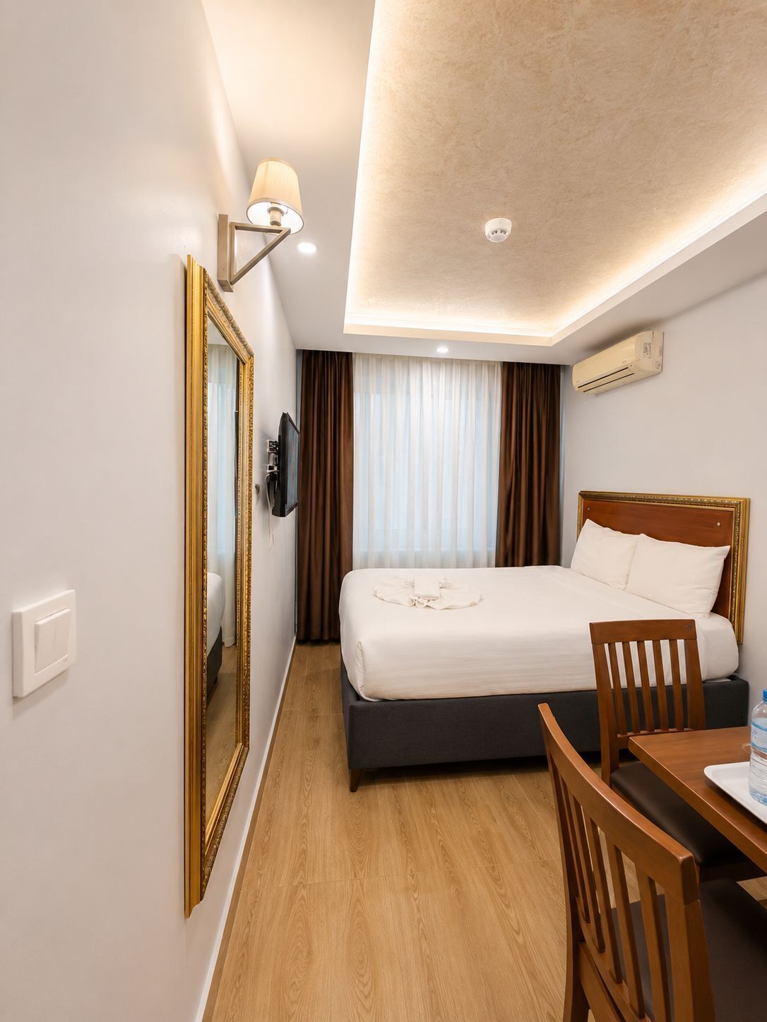 A hotel room with a bed, bedside table, chair, and a mirror.