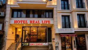 Un hotel llamado 'HOTEL REAL LIFE' con un letrero de 'GLORIA PERFUME' al otro lado de la calle.