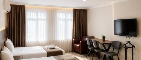 A hotel room with two beds, a desk, a TV, and a chair.