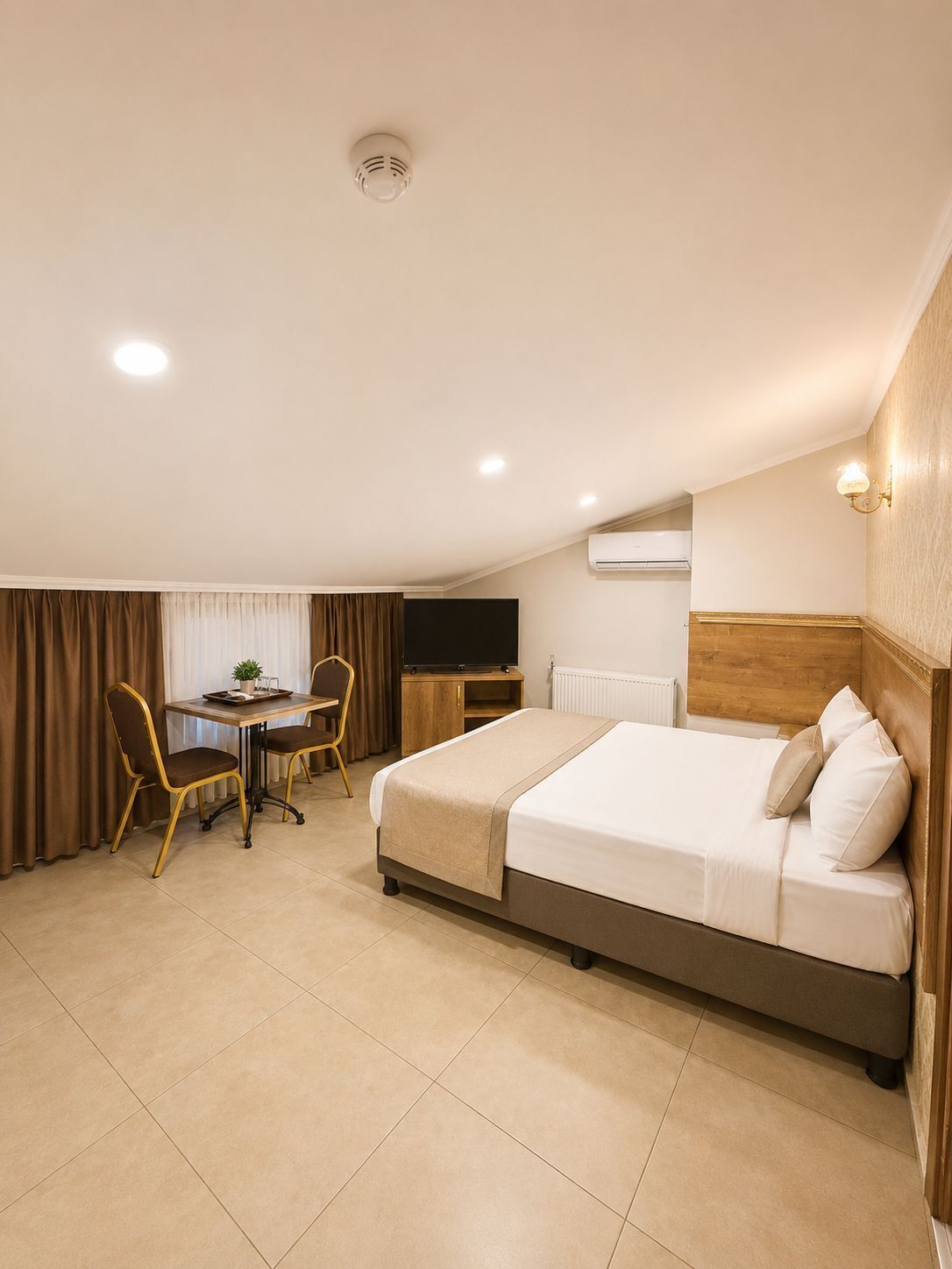A hotel room with a bed, a desk with a chair, a television, and an air conditioning unit.
