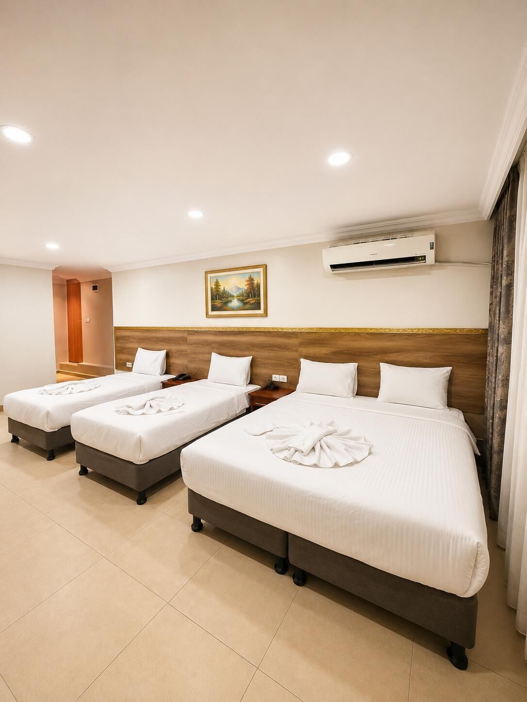 Une chambre d’hôtel avec trois lits, un appareil de climatisation, un tableau et une tête de lit en bois.