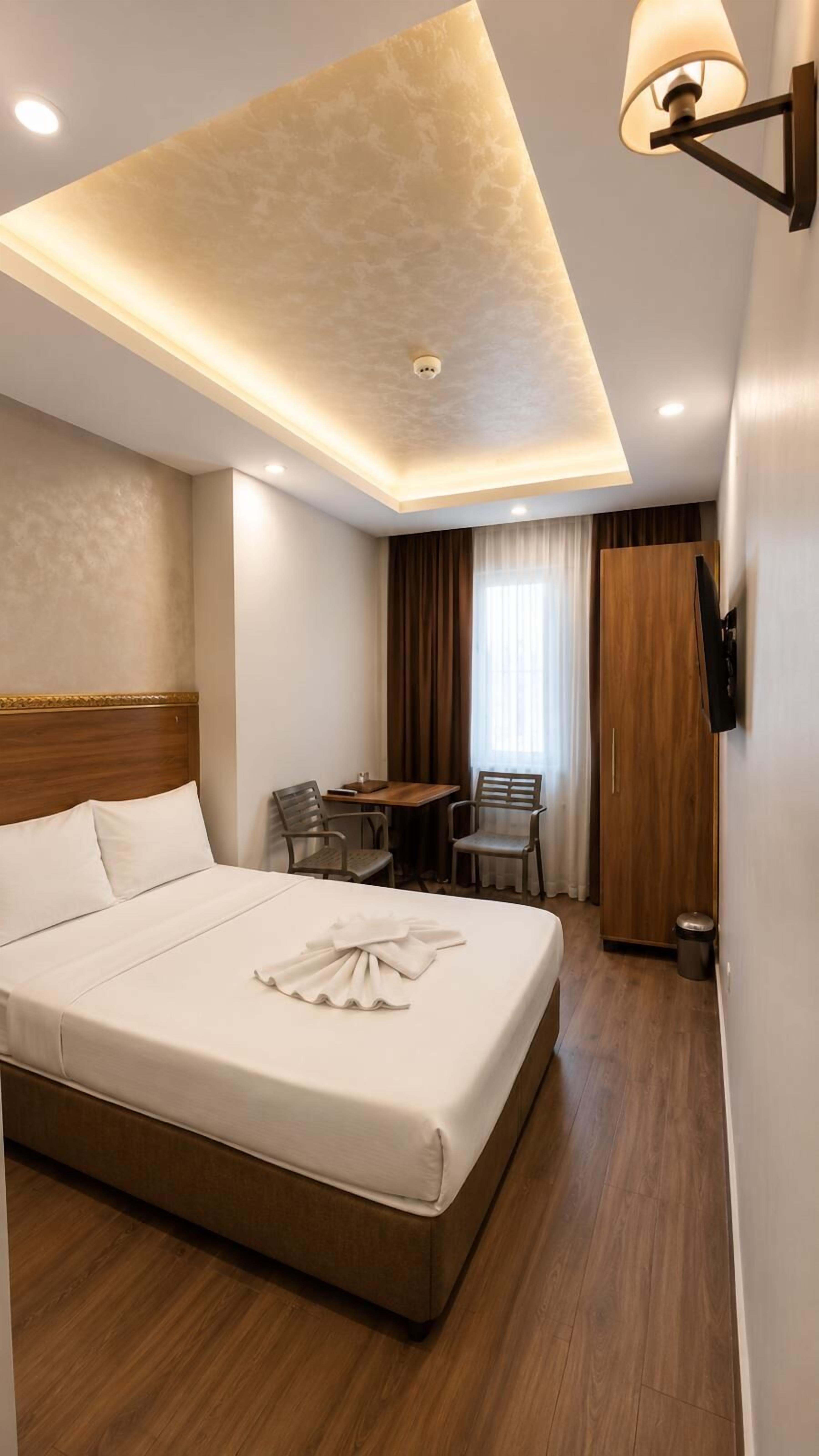 A hotel room with a bed, a desk, chairs, a TV, and a ceiling light fixture.