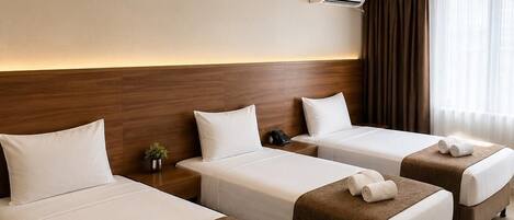 A hotel room with three beds, a wooden headboard, an air conditioning unit, and a small plant on the nightstand.