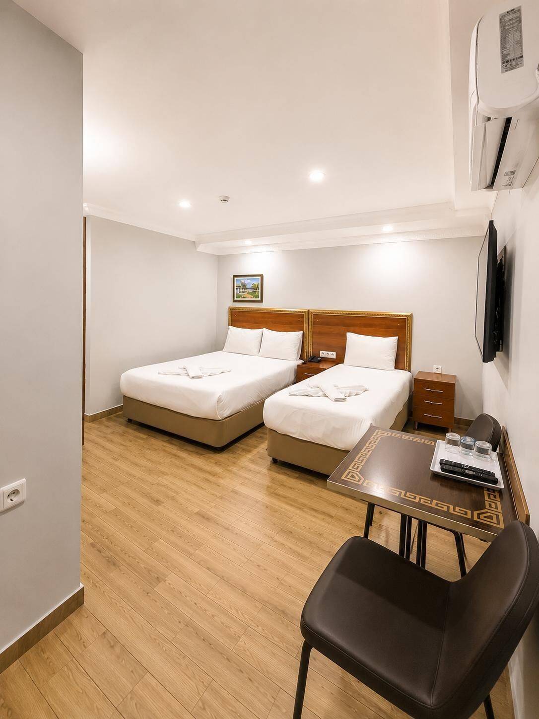 Ein Hotelzimmer mit zwei Betten, einem kleinen Tisch mit Tablett, einem Sessel und einem an der Wand befestigten Fernseher.