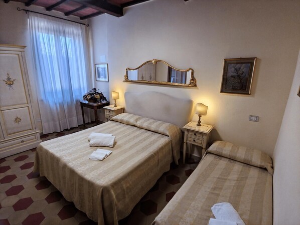 Una habitación de hotel con dos camas, un aparador, un espejo y una mesita de noche con lámpara.