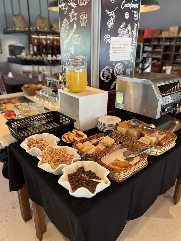 A buffet table with various food items including cereals, pastries, and a juice dispenser.